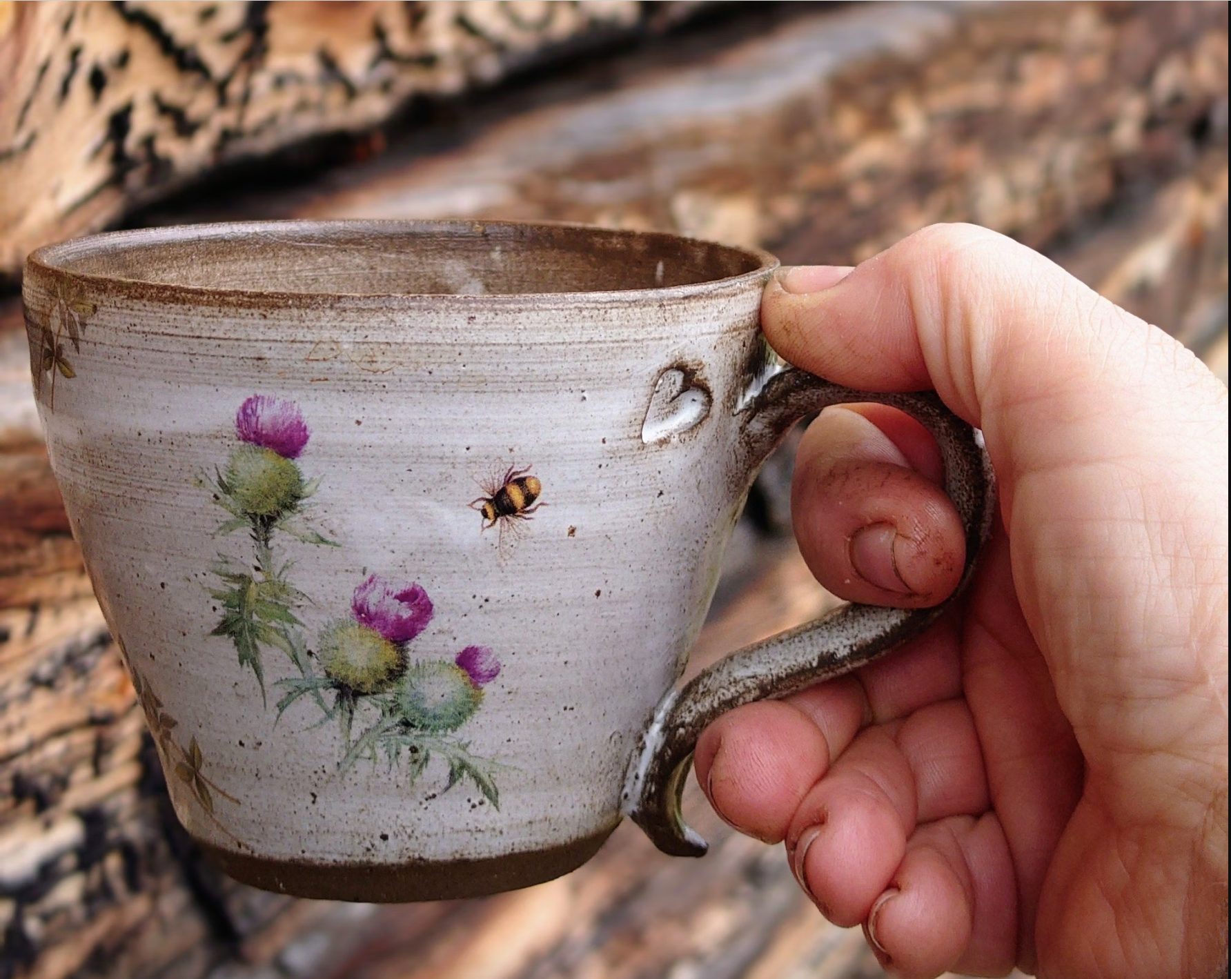 En hand som håller i en kopp tillverkad av keramik med blomster motiv